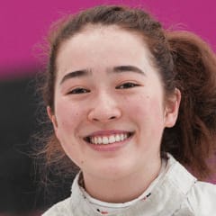 A woman wearing a fencing uniform smiles