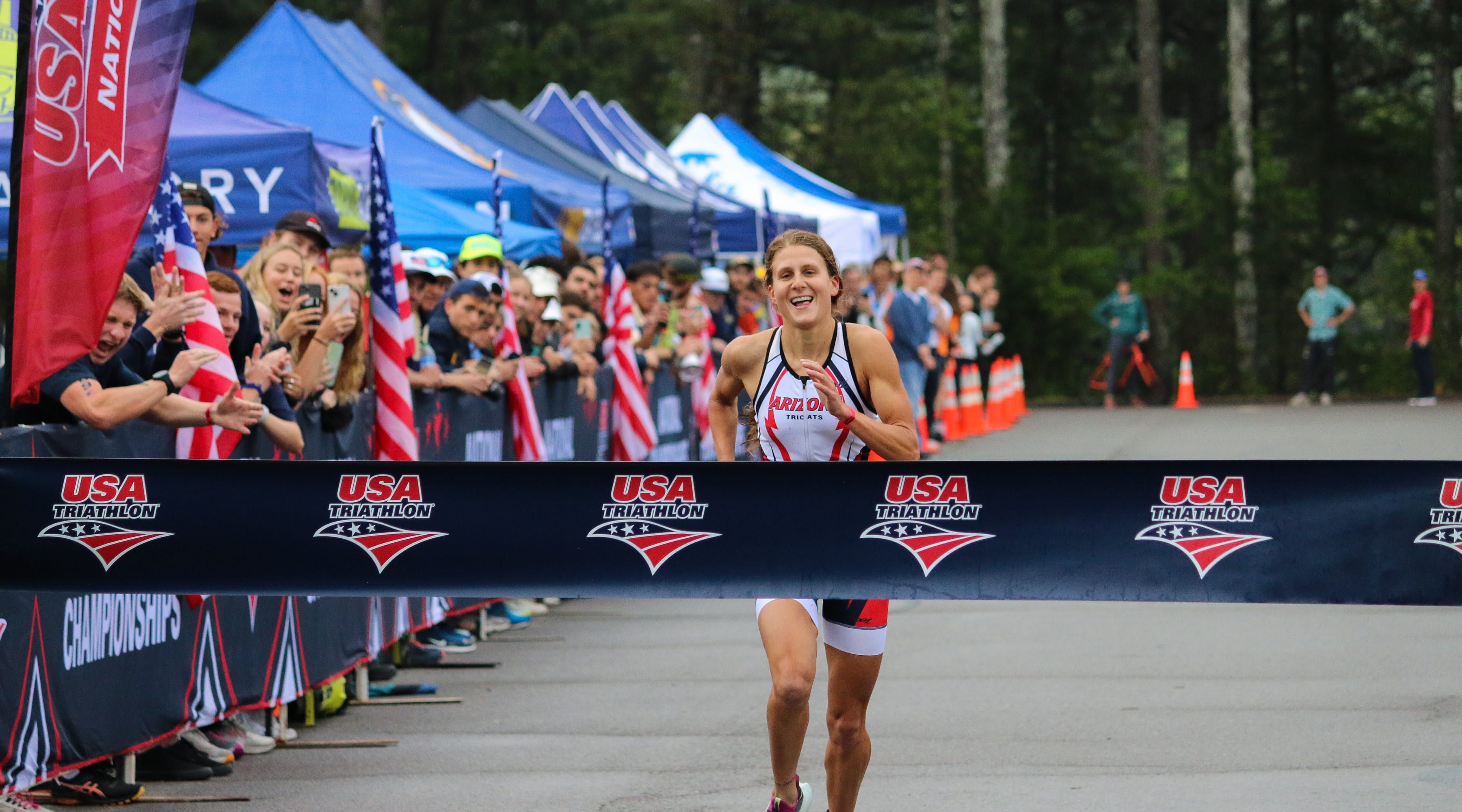 An athlete smiles as she approaches the finish line. The winner's tape is stretched across the finish line.