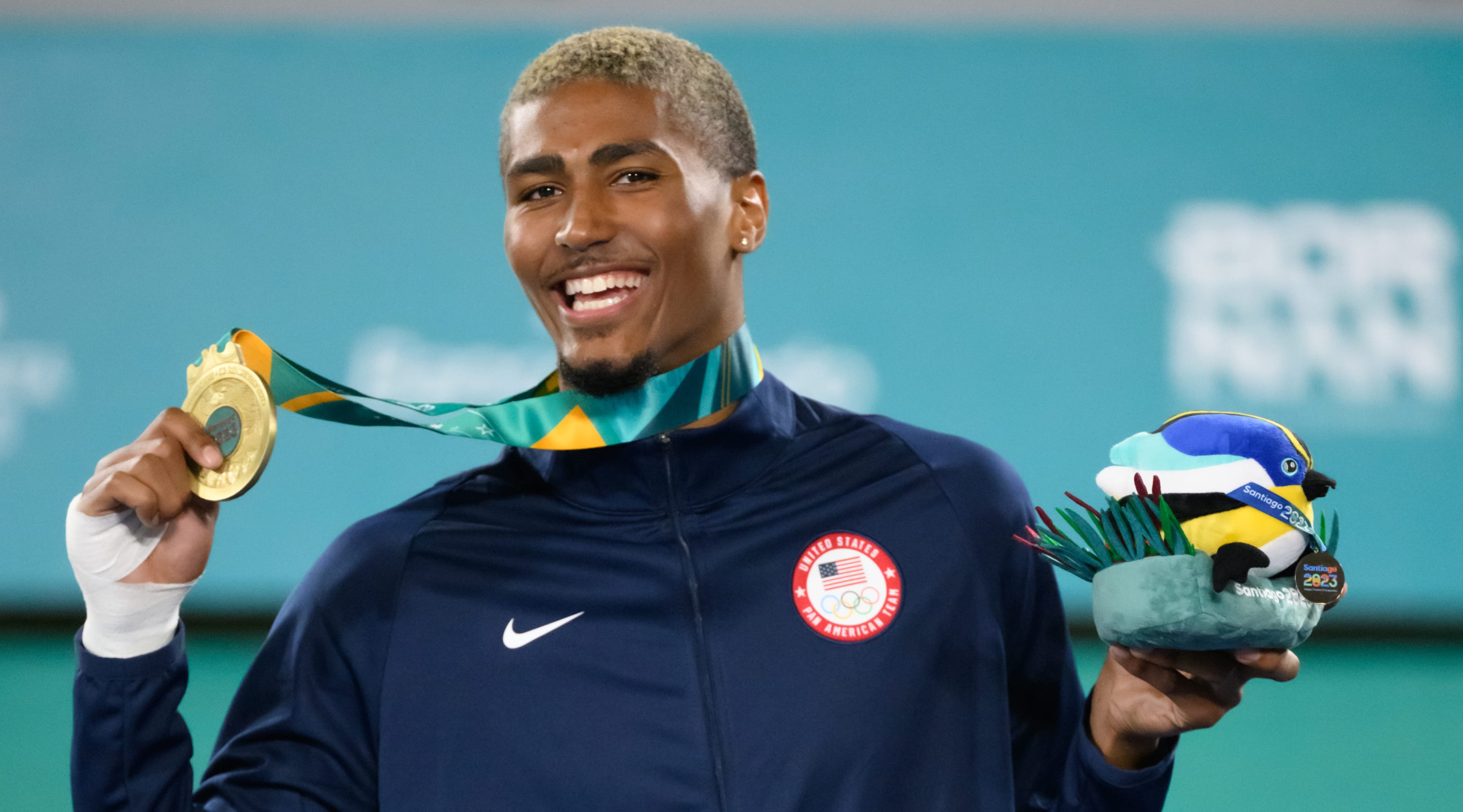 Cj. Nickolas smiling at the camera and holding up his gold medal