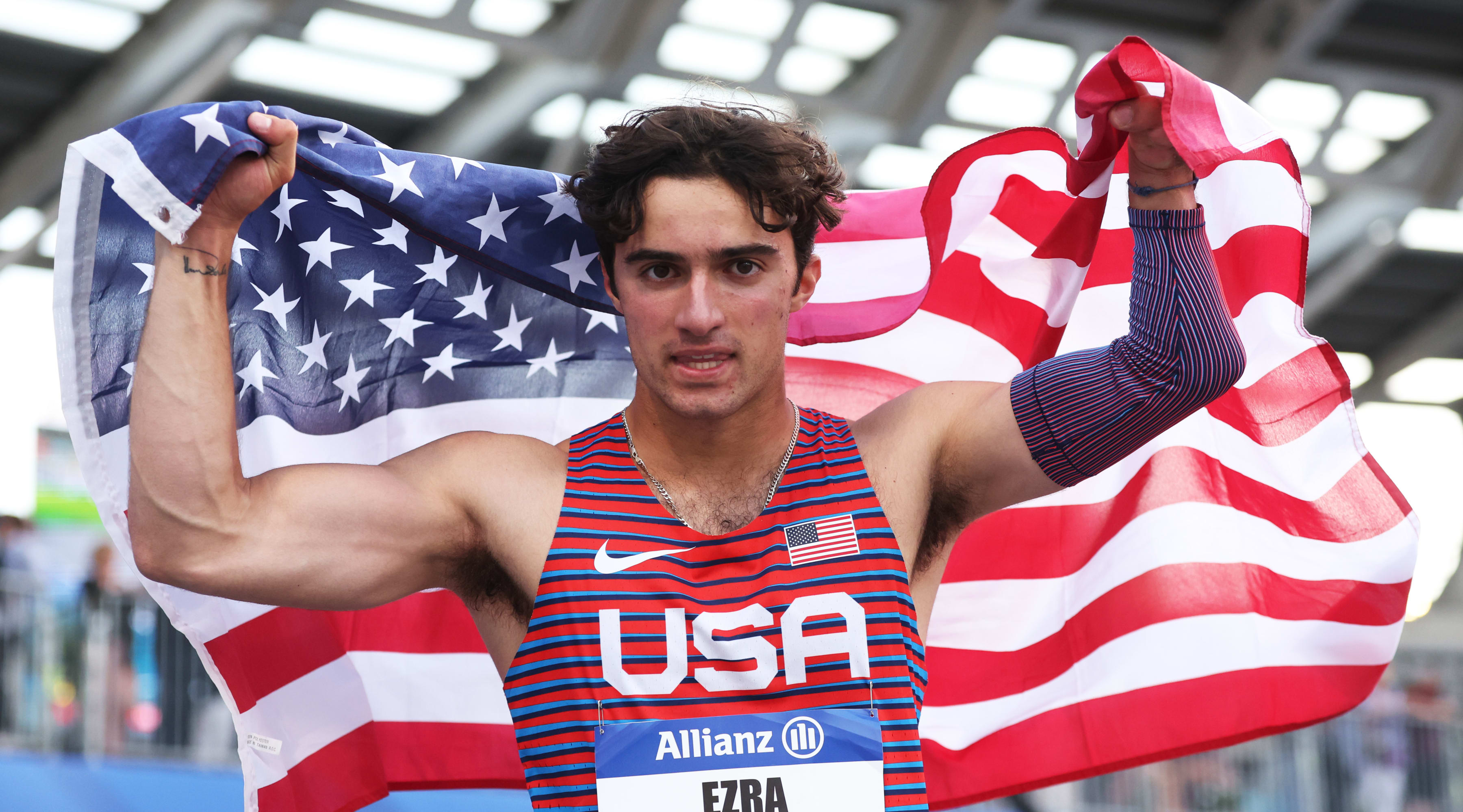 Ezra Frech holds up an American flag behind his back, with a cursive written tattoo visible on the inside of his right wrist.