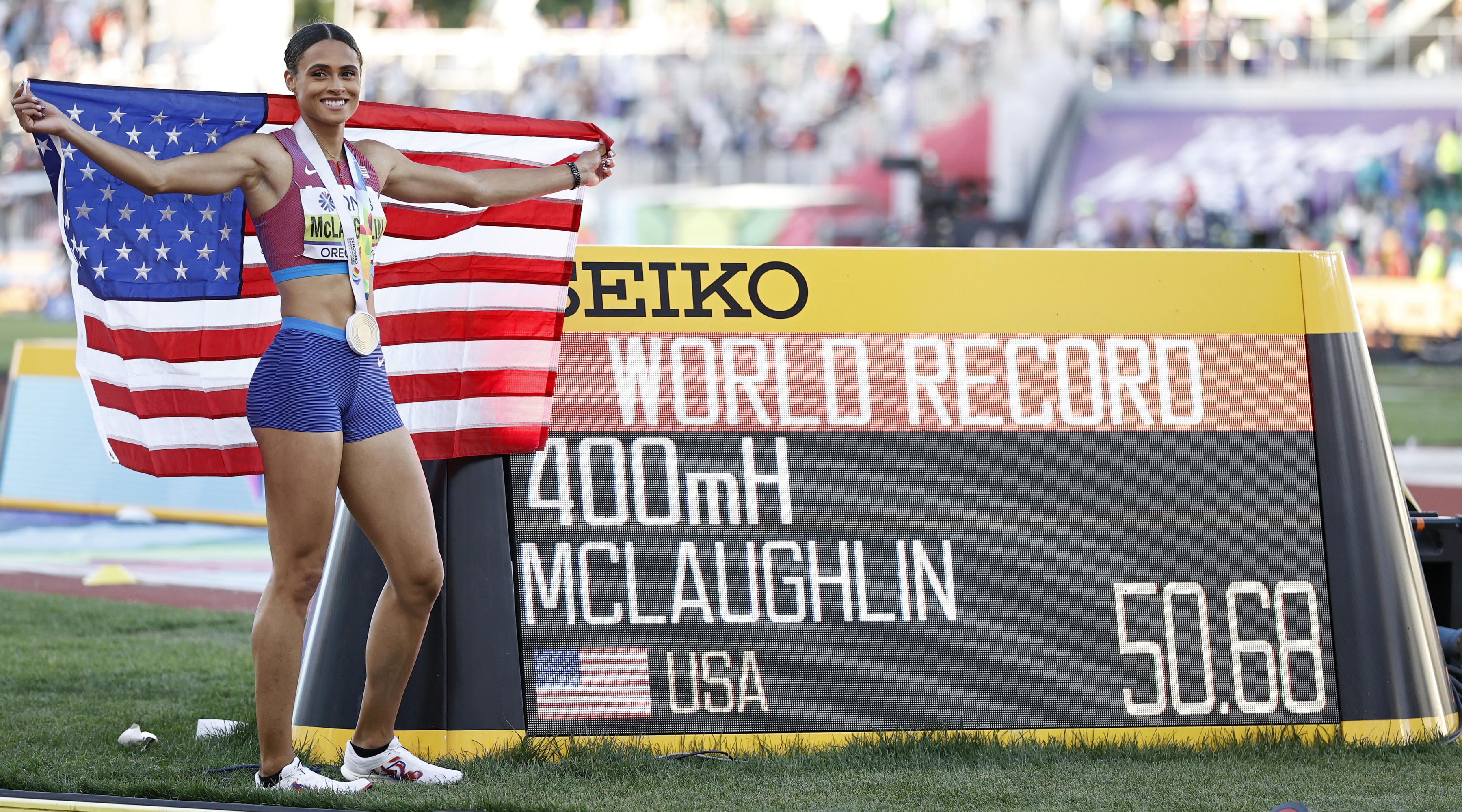 Sydney McLaughlin smiling next to the time board.