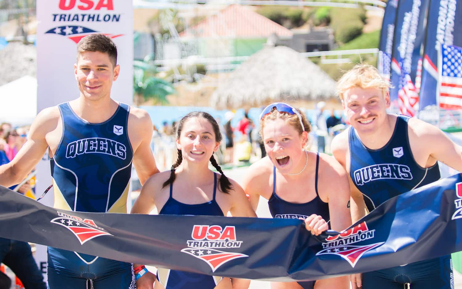 four collegiate triathletes stand together holding the finish tape