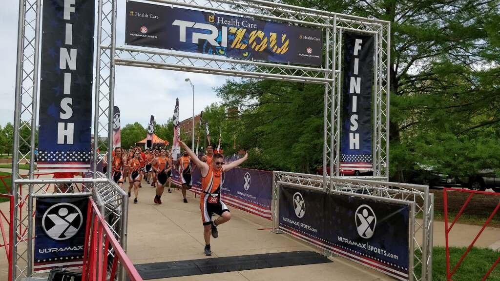 triathlete gabriel cobb crosses the finish line with his arms outstretched