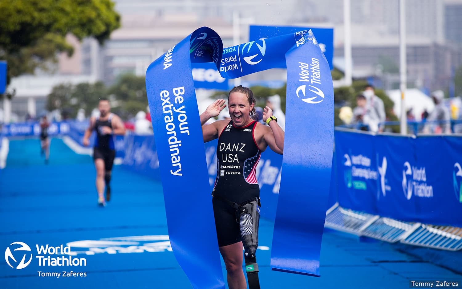 paratriathlete Hailey Danz crosses the finish line with the finish tape above her head and she is smiling