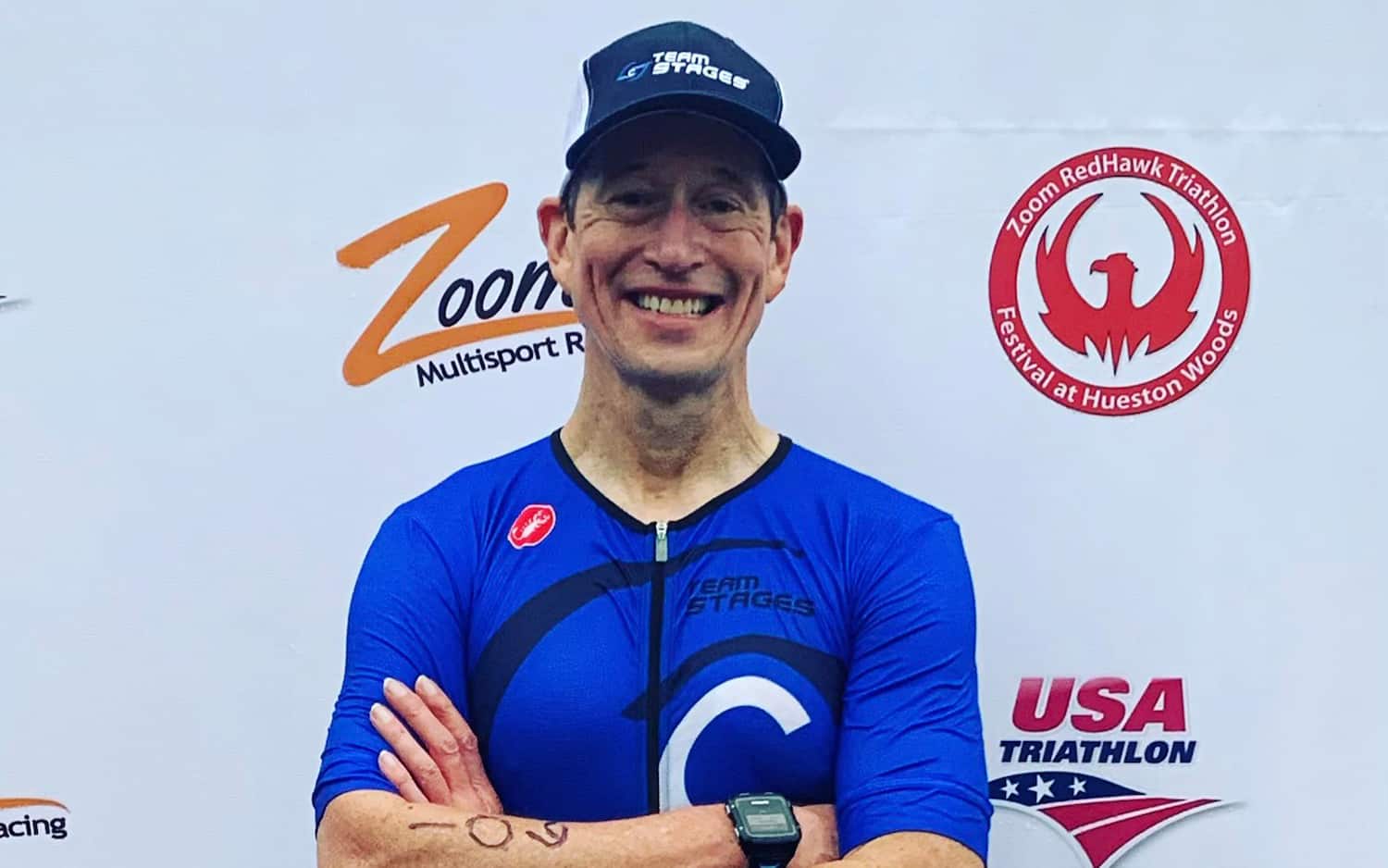 Bruce Miller smiles an dstands in front the Zoom RedHawk Triathlon Festival's photo backdrop.