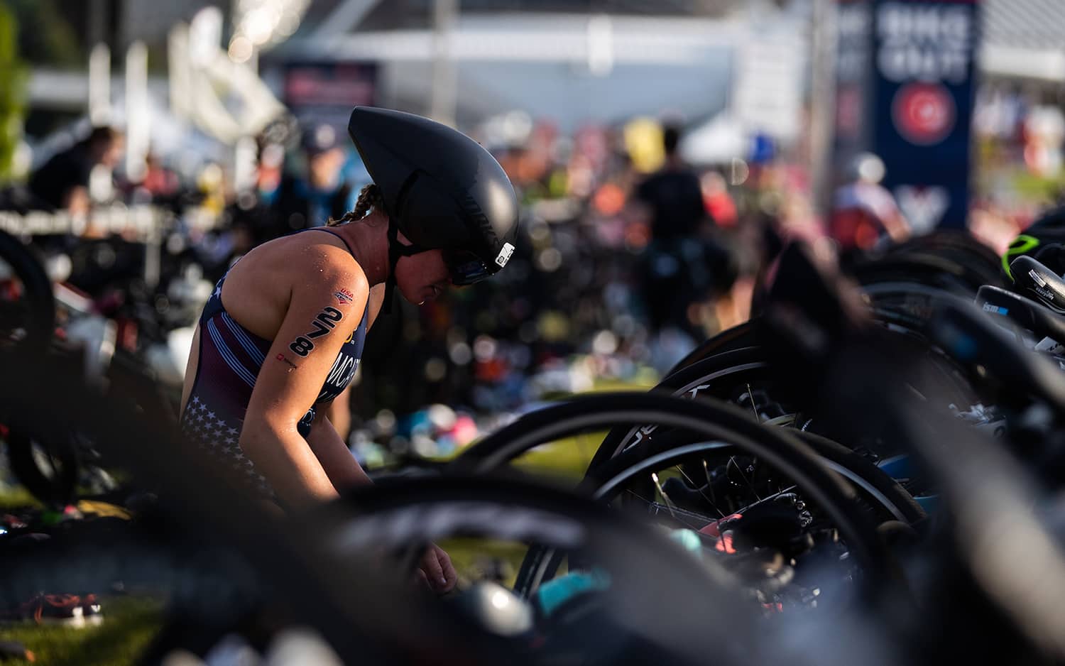 An athlete, wearing a helmet, readies herself for the cycling portion of a race in the transition area.