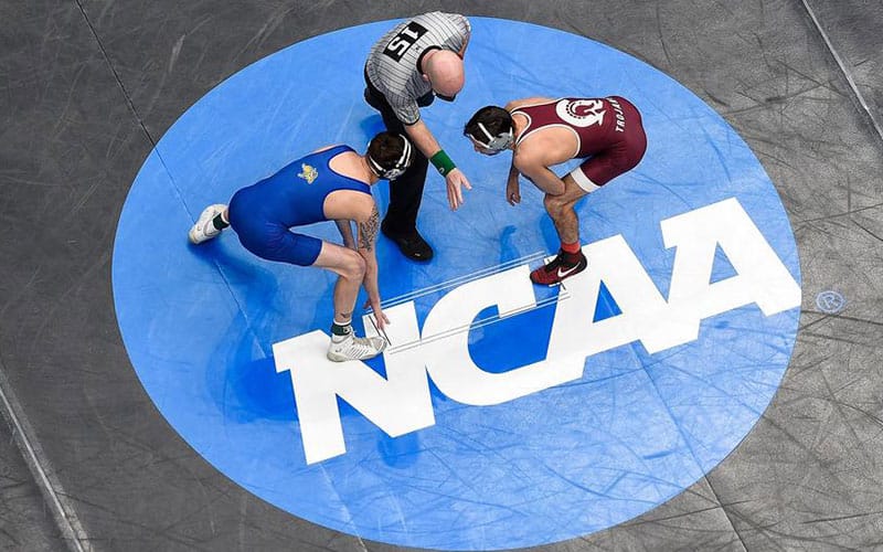 NCAA wrestling mat with athletes and referee