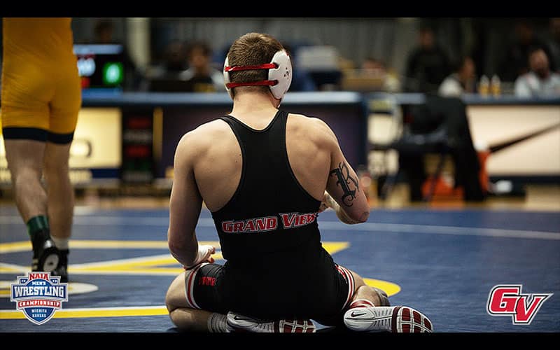 A Grand View wrestler sits on the mat, with photo showing back of his singlet.