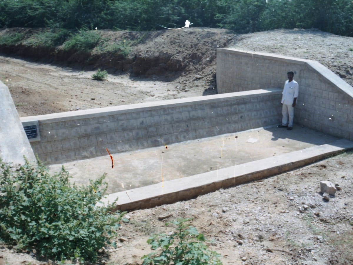 A man standing inside a newly built masonry water-harvesting structure cut into an earth bank