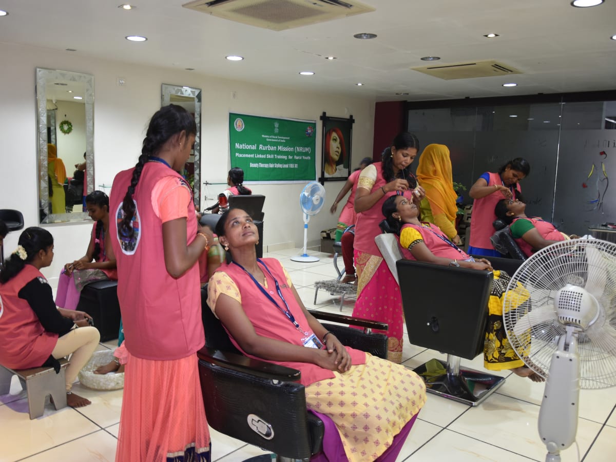 Trainees in aprons practising hair washing and styling on one another at salon chairs