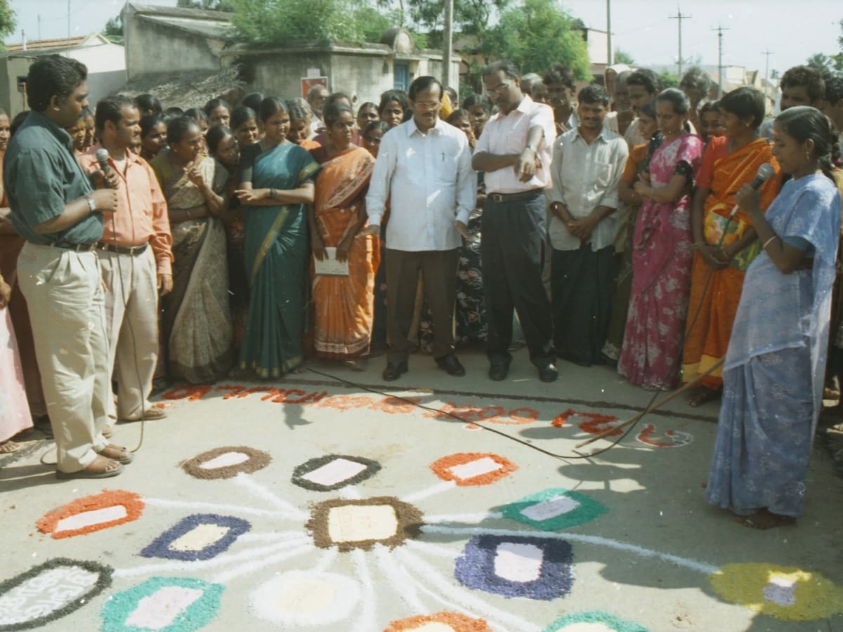 A woman speaking into a microphone beside a large coloured diagram laid out on the ground