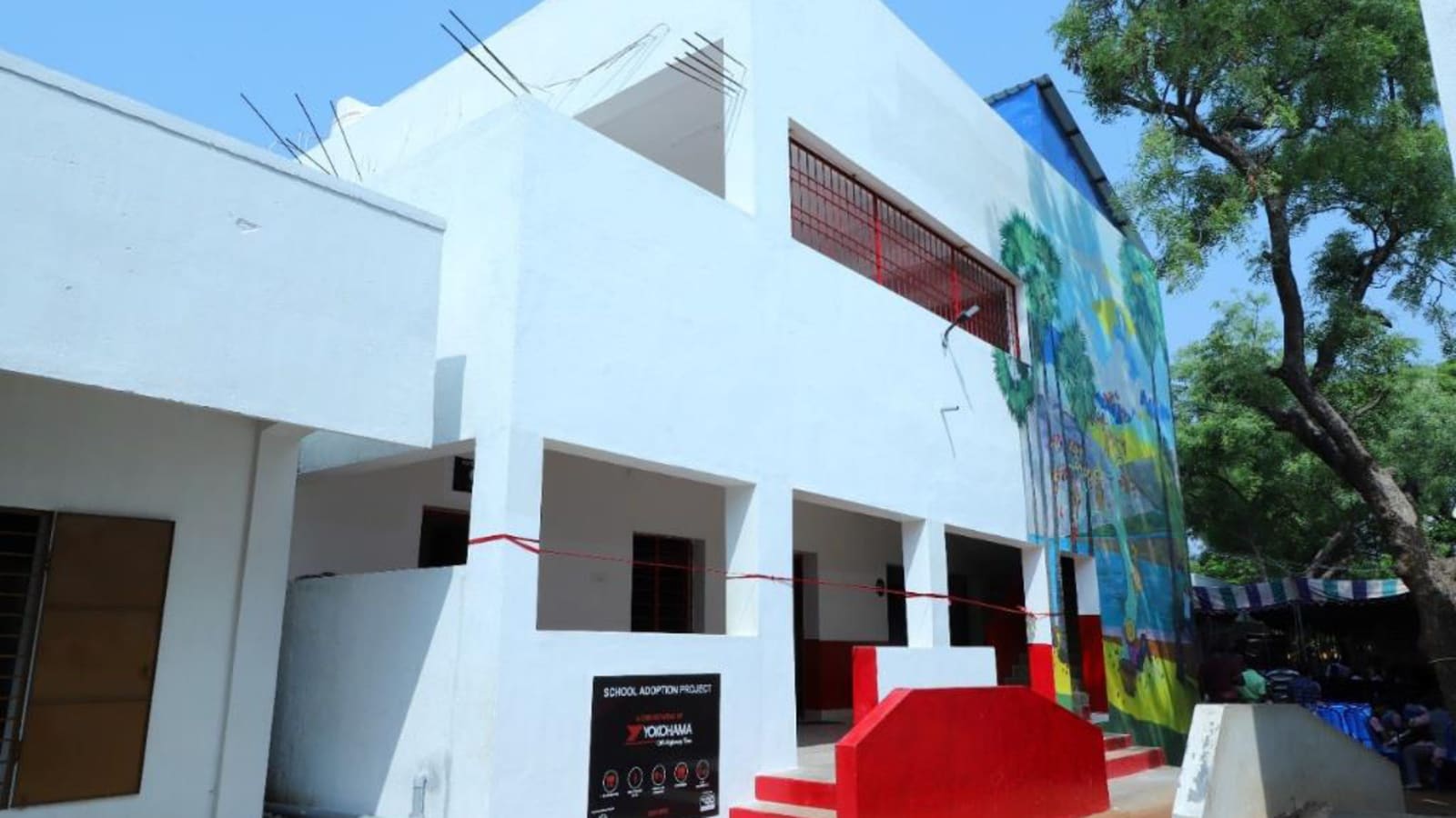A two-storey school building with a red exterior staircase and a painted wall mural on one side