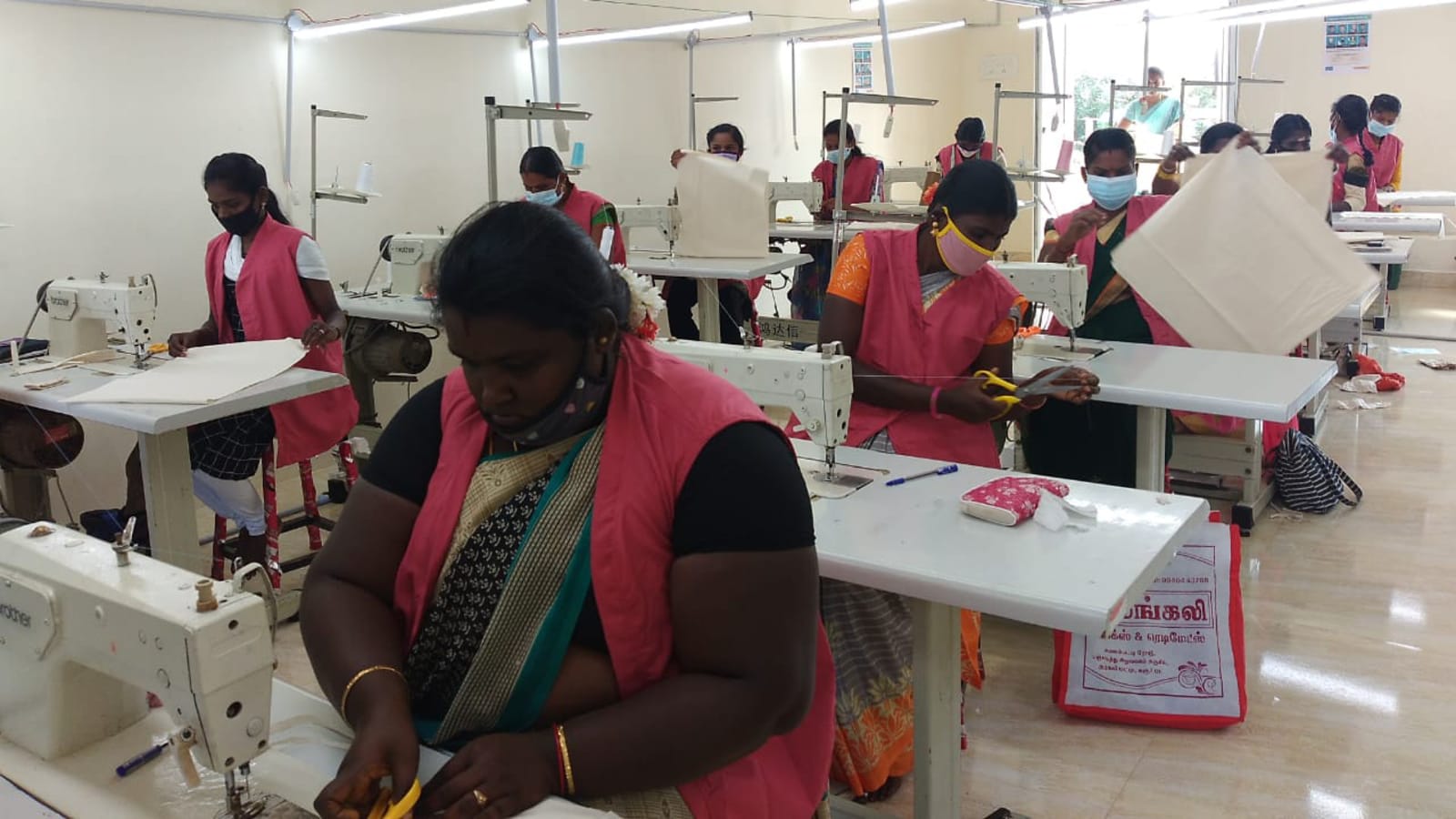 Women in training vests working at industrial sewing machines in a tailoring workshop