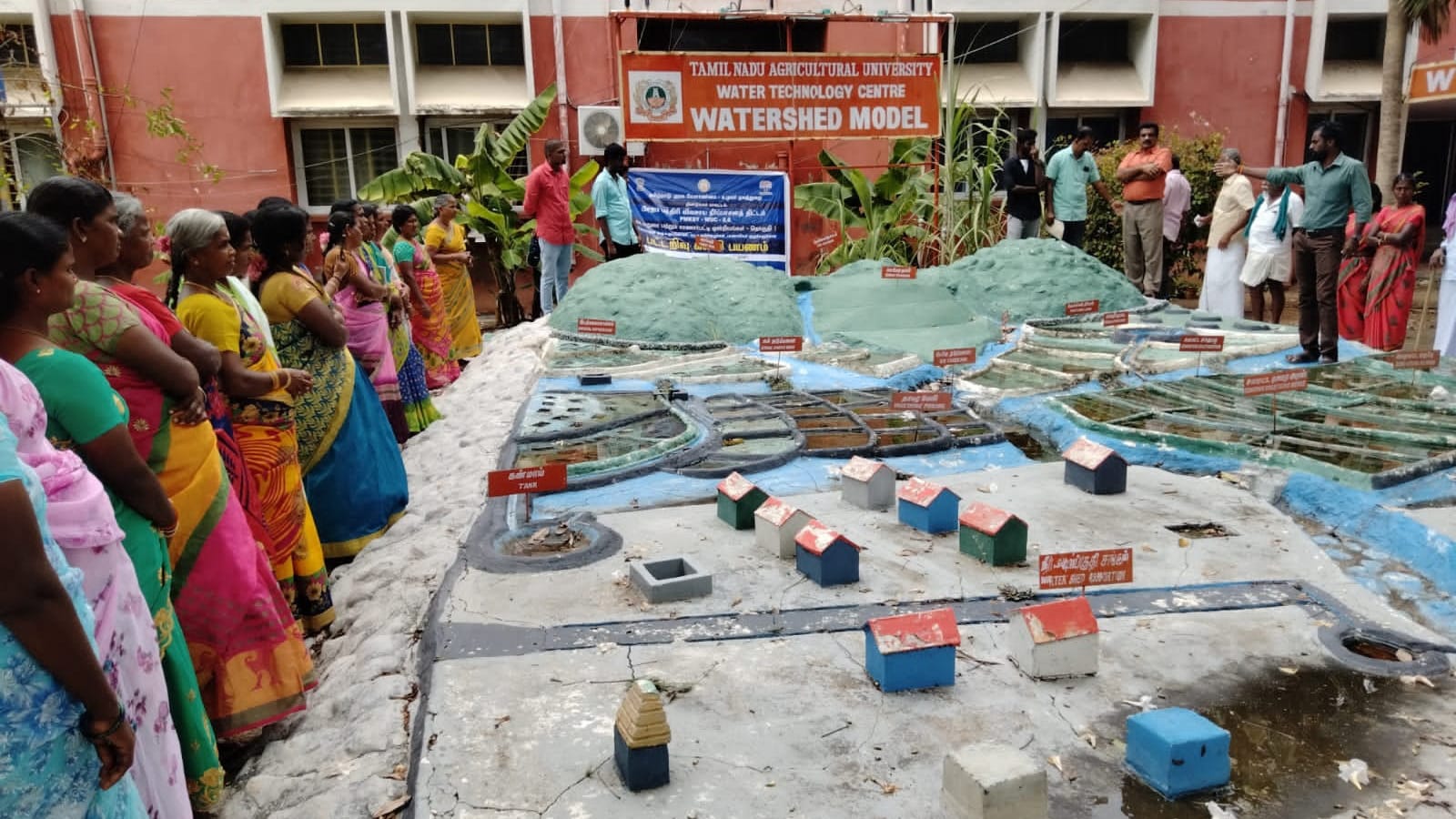 Women standing along the edge of a large outdoor scale model of a watershed with miniature structures laid out across it