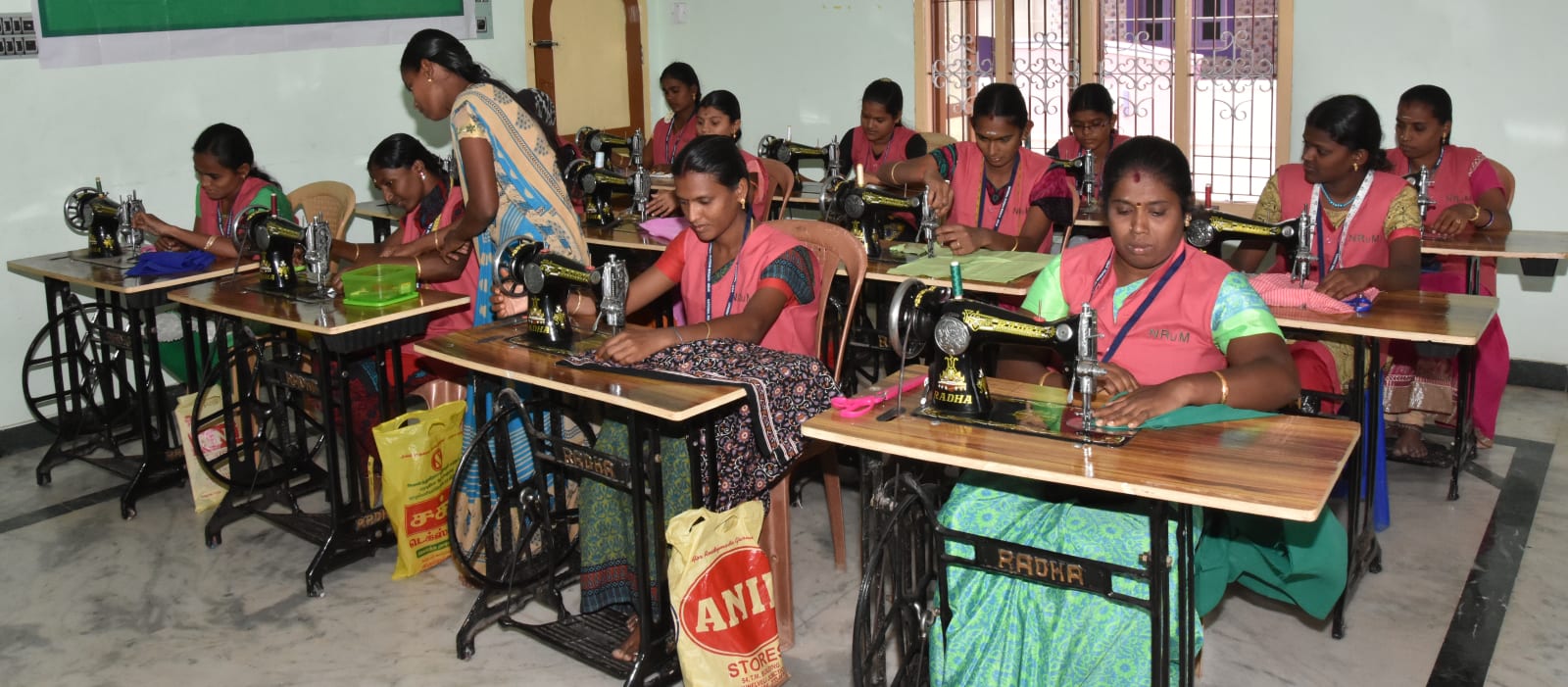 Women trainees at rows of treadle sewing machines in a vocational tailoring hall