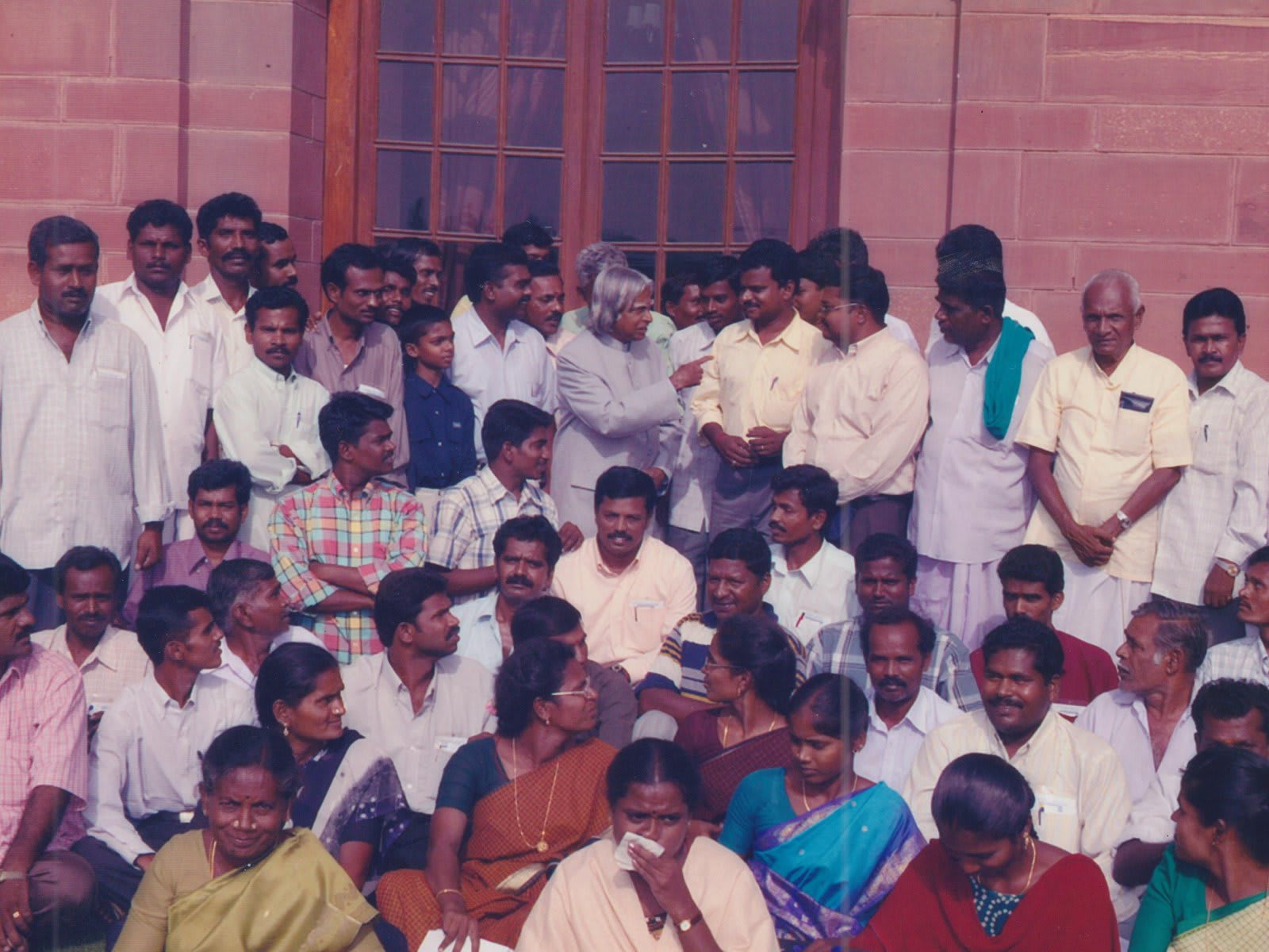 A dense group of men and women standing close together outdoors in front of a red sandstone wall, Dr A. P. J. Abdul Kalam in white among them