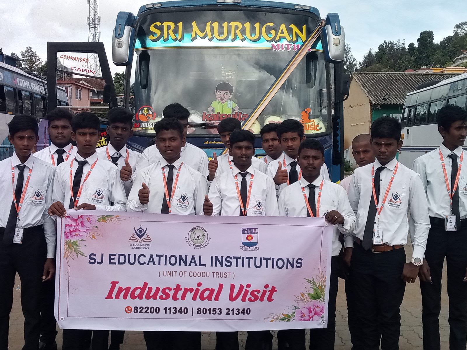 Two rows of students in white shirts, black trousers and ties standing in front of parked coaches, holding a pink banner reading Industrial Visit