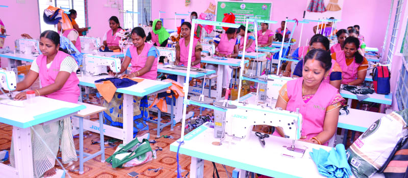 Women in aprons work at rows of industrial sewing machines in a training hall