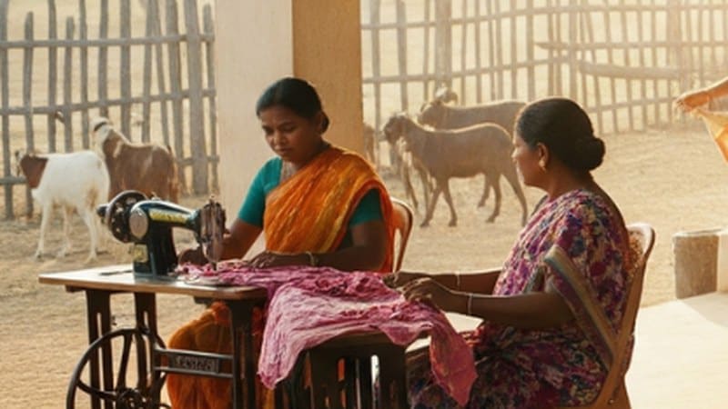 Two women working at a treadle sewing machine in a courtyard workspace
