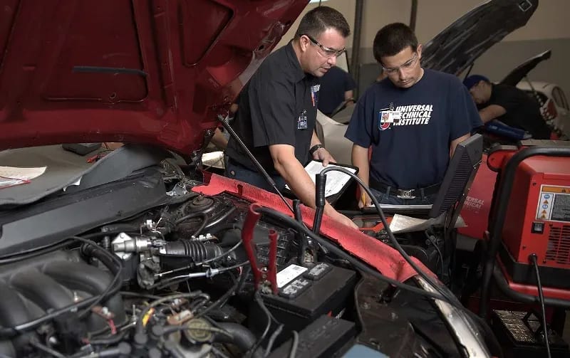 An instructor helps a student check a vehicle's battery in a UTI lab.