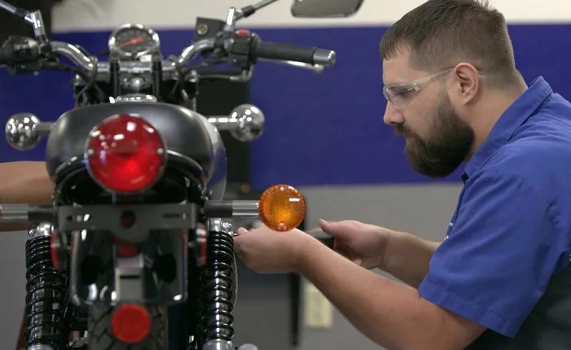 A motorcycle student makes an adjustment to a bike in an MMI lab.