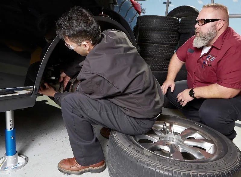 An Automotive instructor helps a student adjust a vehicle's suspension in a UTI lab.