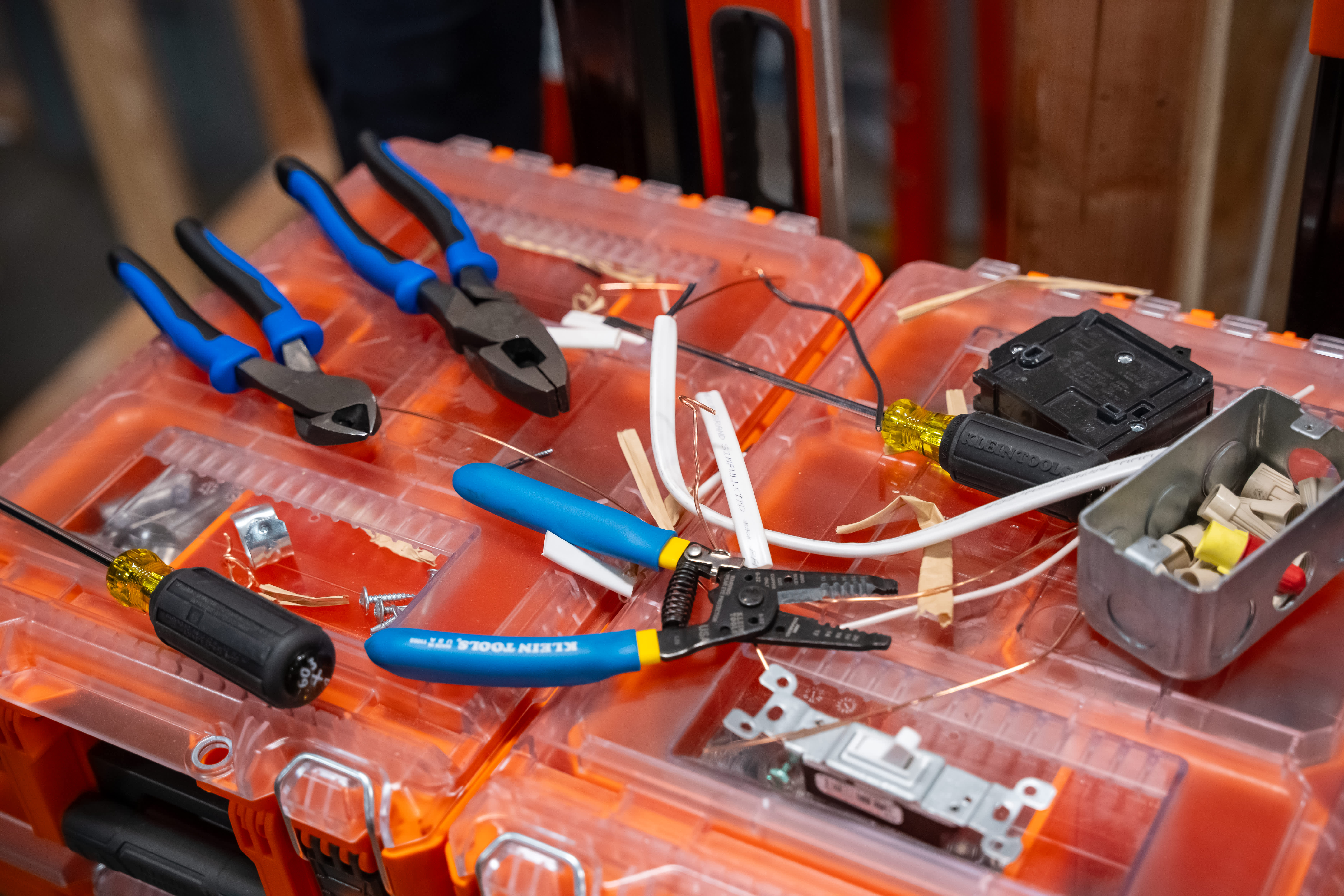 Orange toolboxes hold various hand tools, electrical wiring, and hardware components.