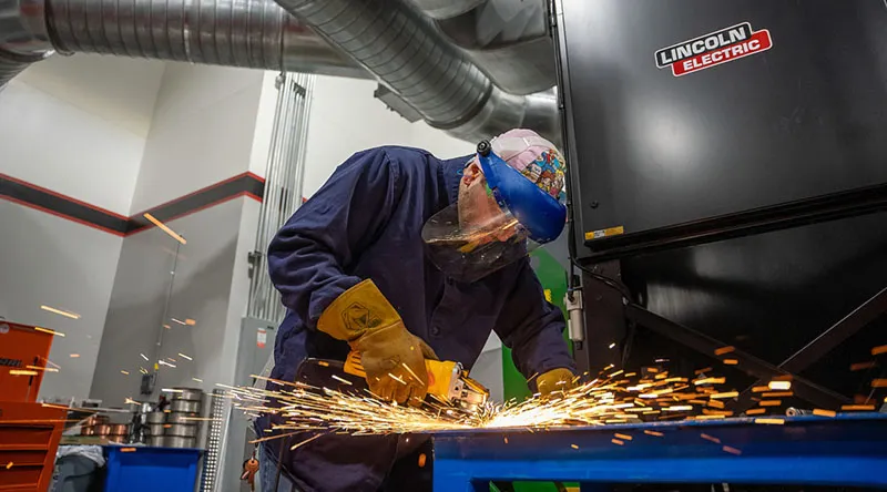 A welder using a large welding machine in a manufacturing environment.
