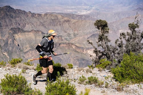 A man running in the Hajar mountains with full kit of ultra running