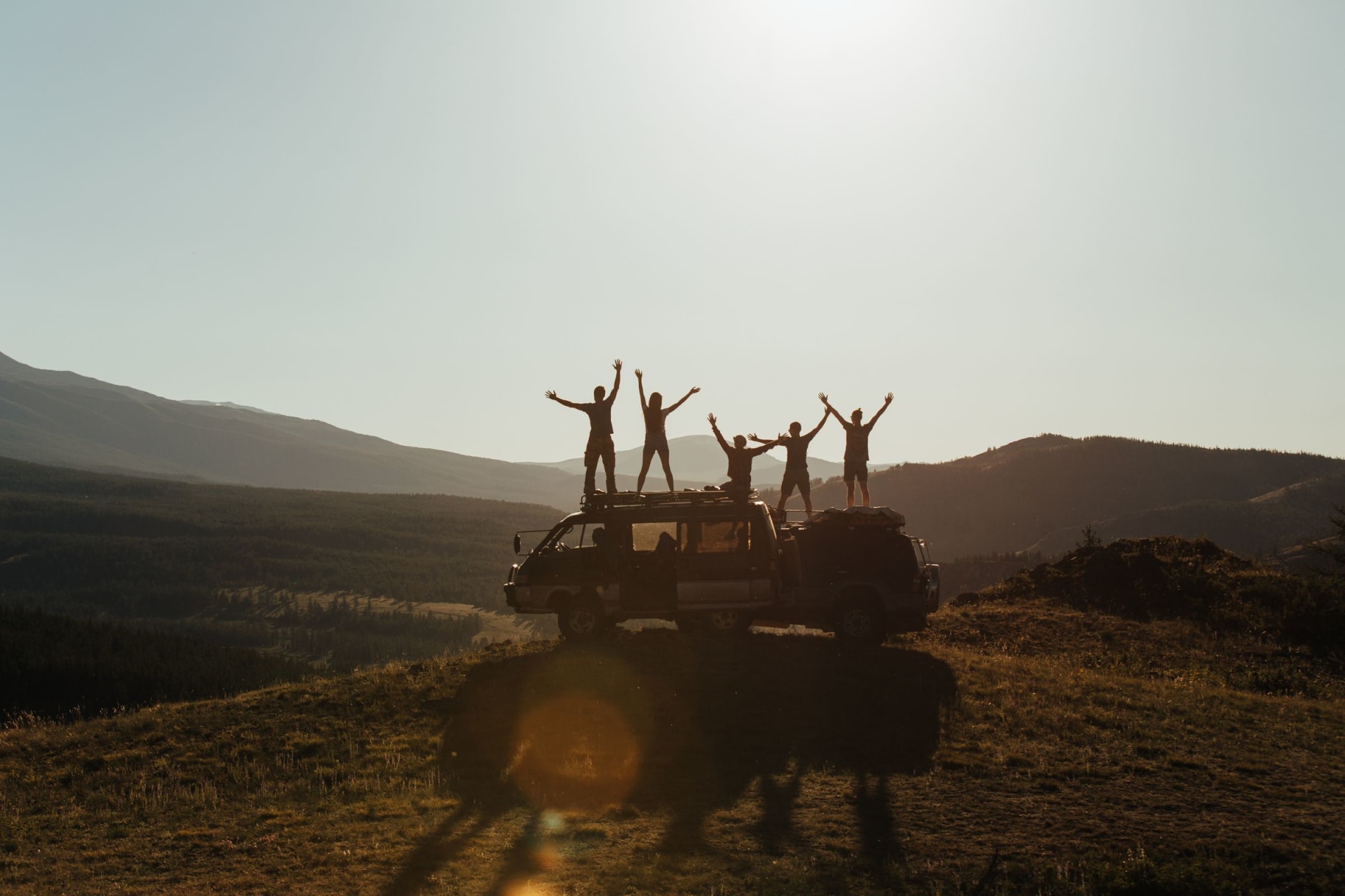 Happy travellers cheering on the roof of their car at a mountain viewpoint at sunrise