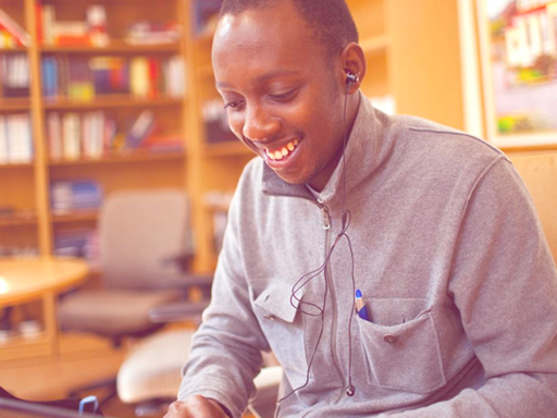 Student sitting at a desk on a computer smiling with a bookshelf in the background