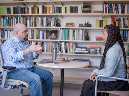 Man and woman sitting at a table talking with bookshelves in the background