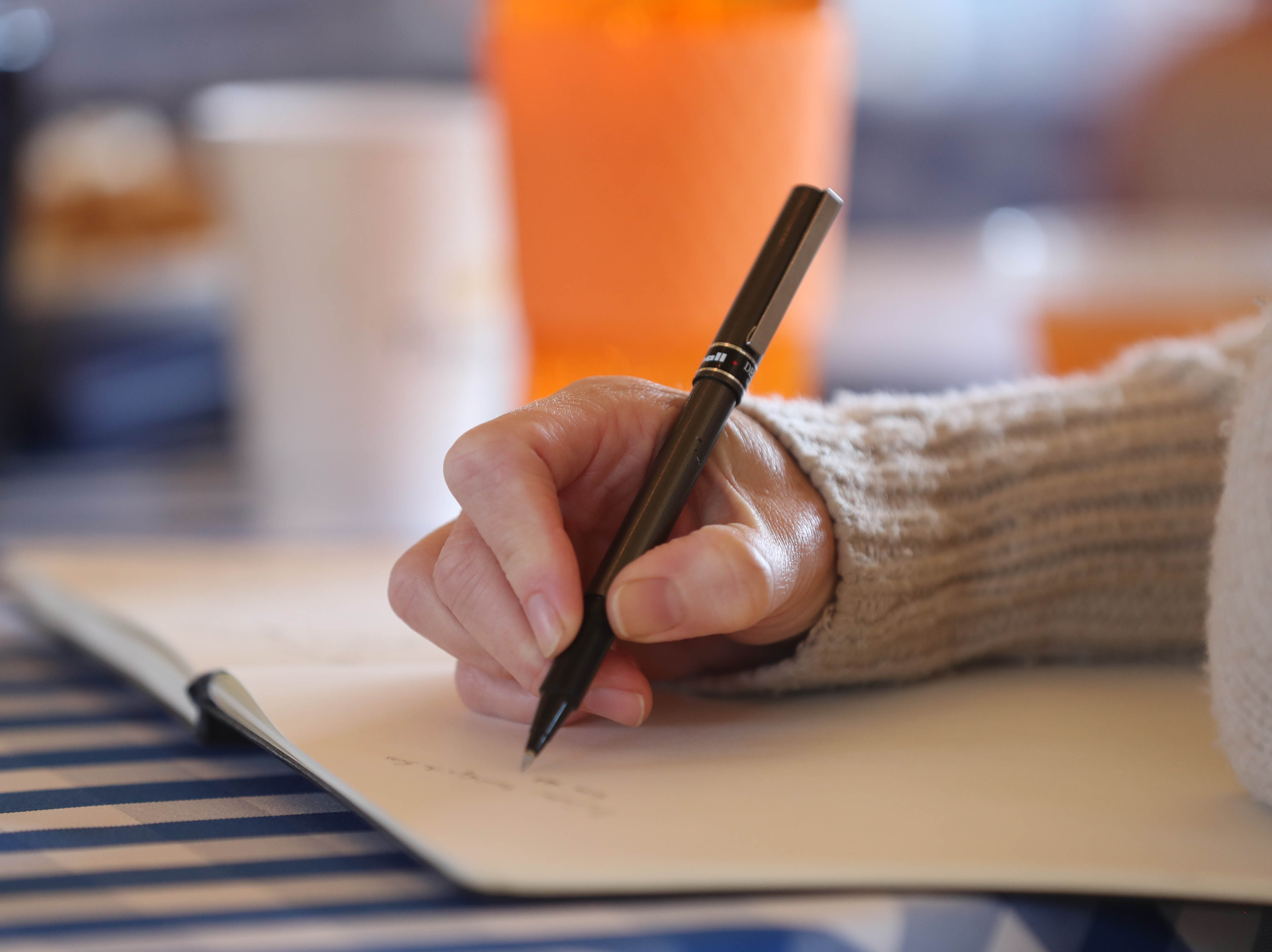 Female student with a beige sweater writing in a notebook with a pen