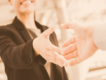 A woman dressed in a business suit smiling and shaking an outstretched hand