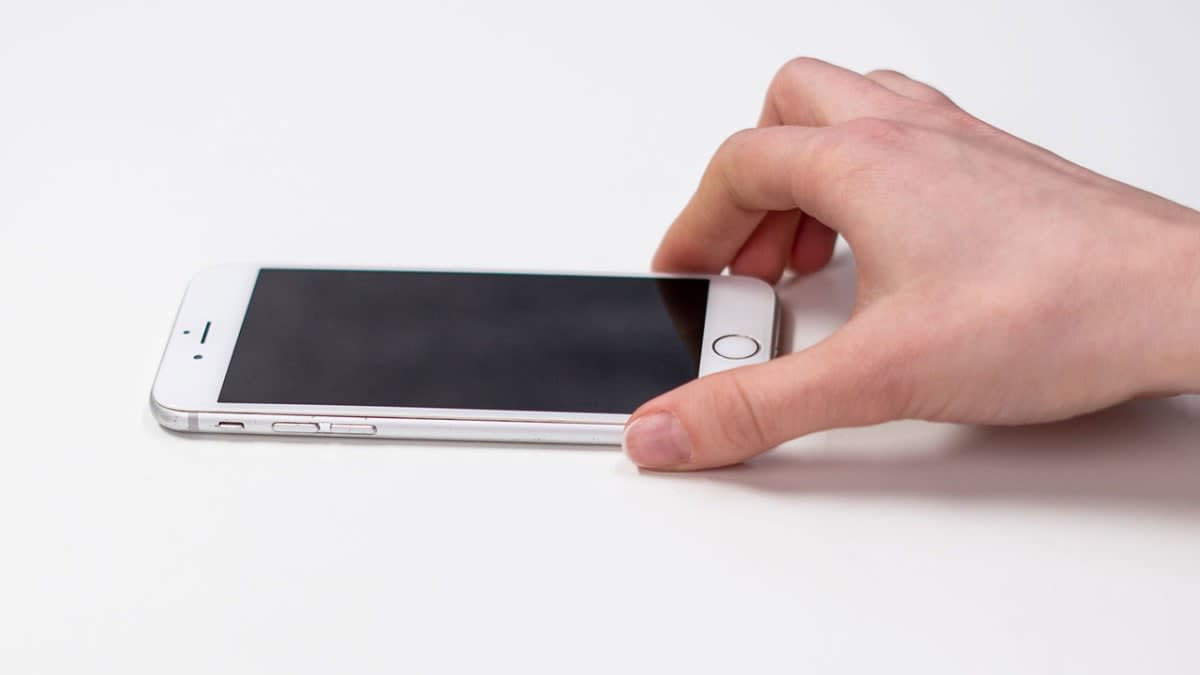 Hand placing a silver iPhone on a white desk beside AirPods, illustrating iPhone 18 Pro NZ price coverage