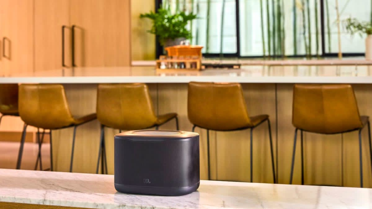 Black JBL Cove X1 Wi-Fi speaker on a marble kitchen bench in front of leather bar stools