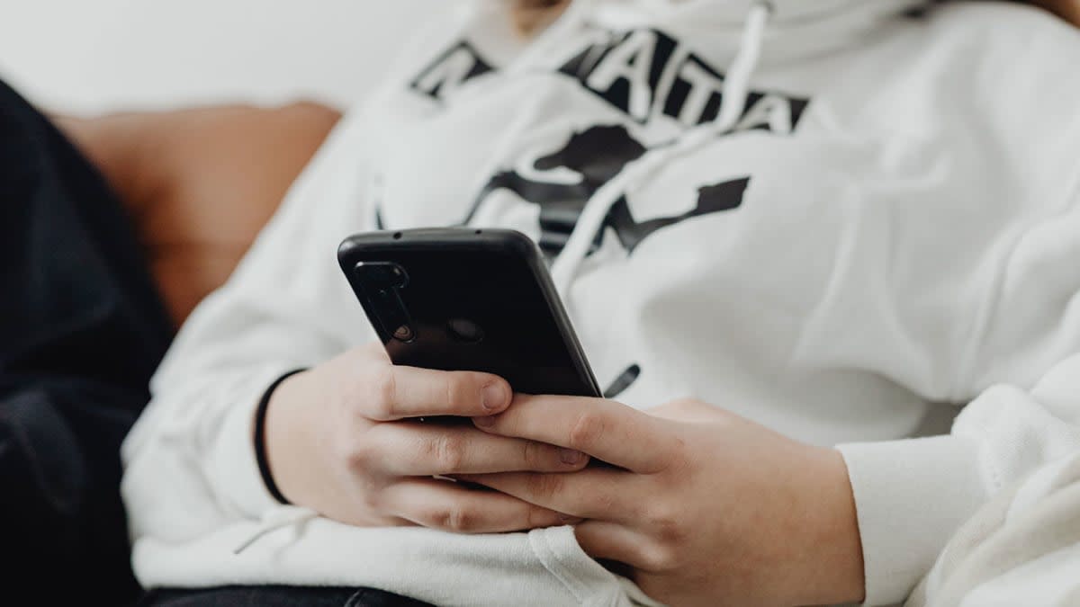 Teenager in a hoodie holding a smartphone, representing existing social media accounts under the proposed NZ ban