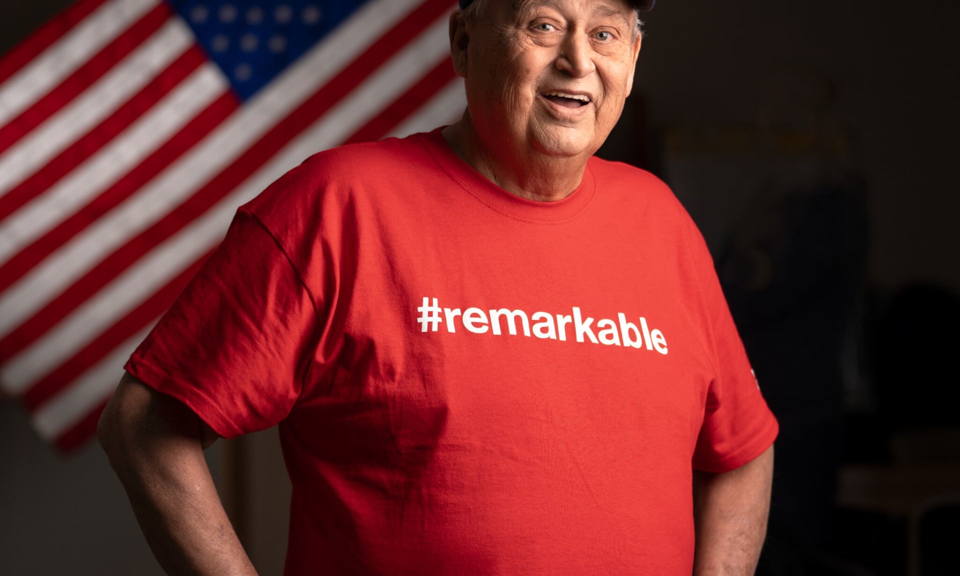 Robert Cole 286564-4385 Man smiling in front of the American Flag wearing US Navy veterans cap
