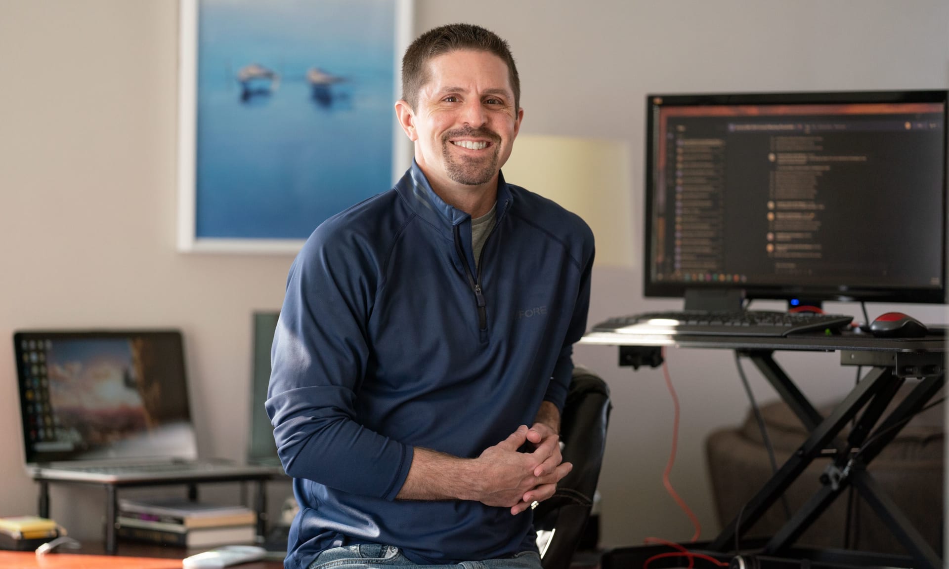 Roman 621145-1092 Jason Roman smiling in his office next to computer desk.