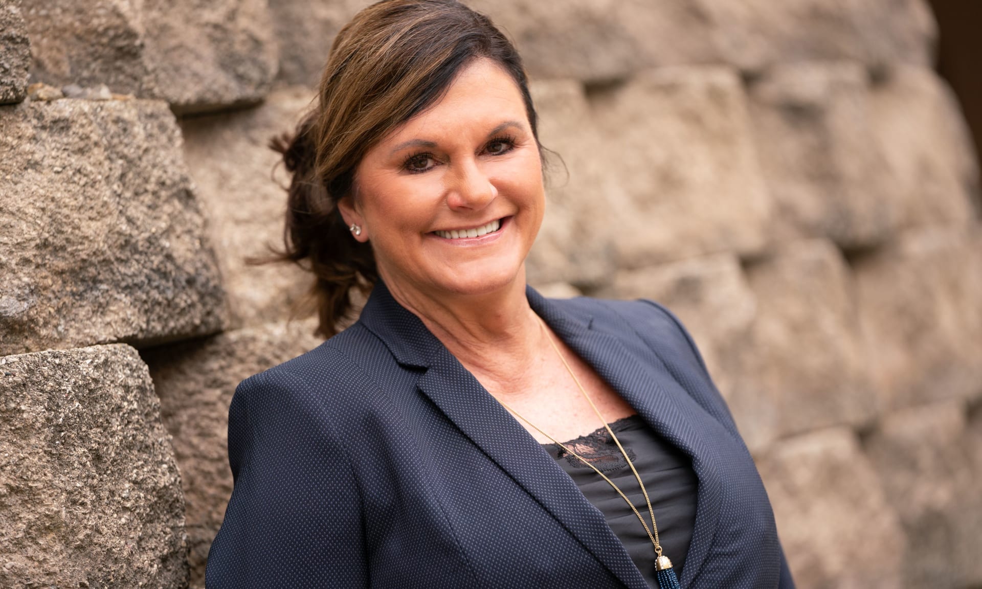Living Donor 247712-2330.jpg Woman outside smiling and leaning against a rock wall.