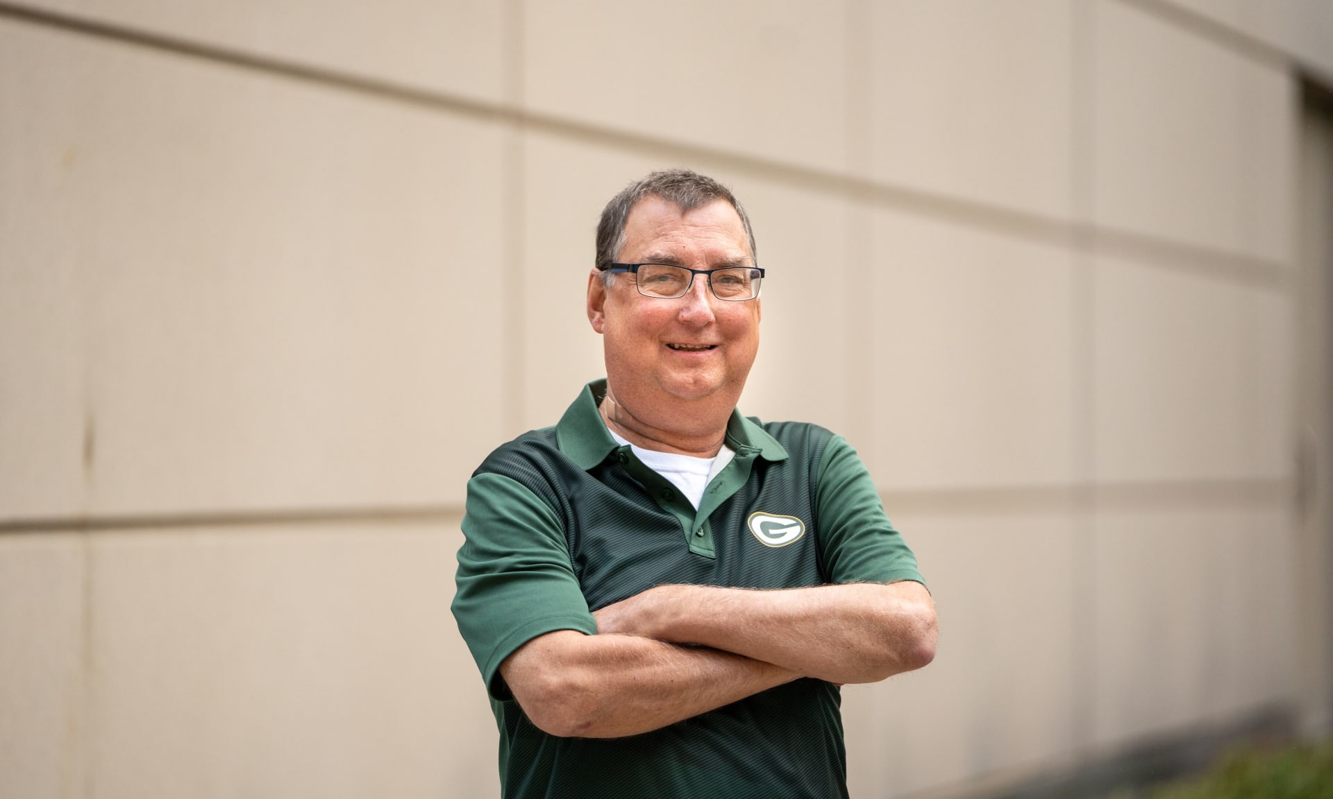 Hartmann 400231-9616.jpg A smiling man wearing a Green Bay Packers shirt standing with his arms crossed