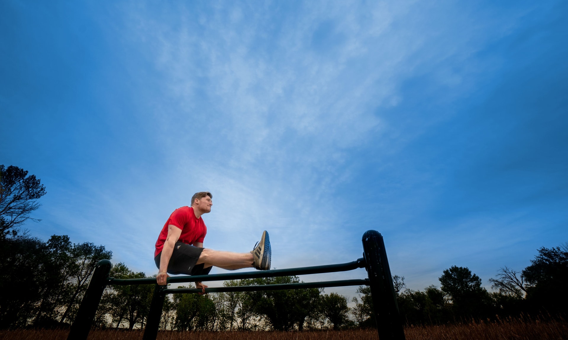McDermott 345478-6268 Young man balancing on hands using parallel bars outdoors.
