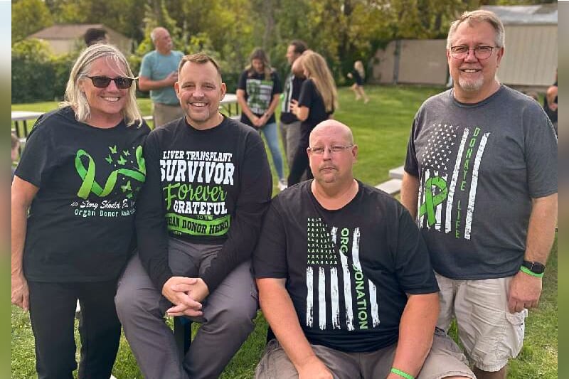 Four adults smiling outdoors, one female and three males.