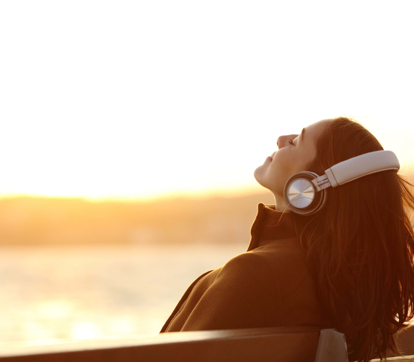 Woman wearing headphones listening to music breathing fresh air relaxing sitting on a bench in winter on the beach