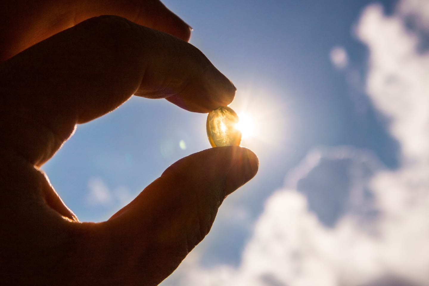 A silhouette of a hand holding up a vitamin D capusle to the sun