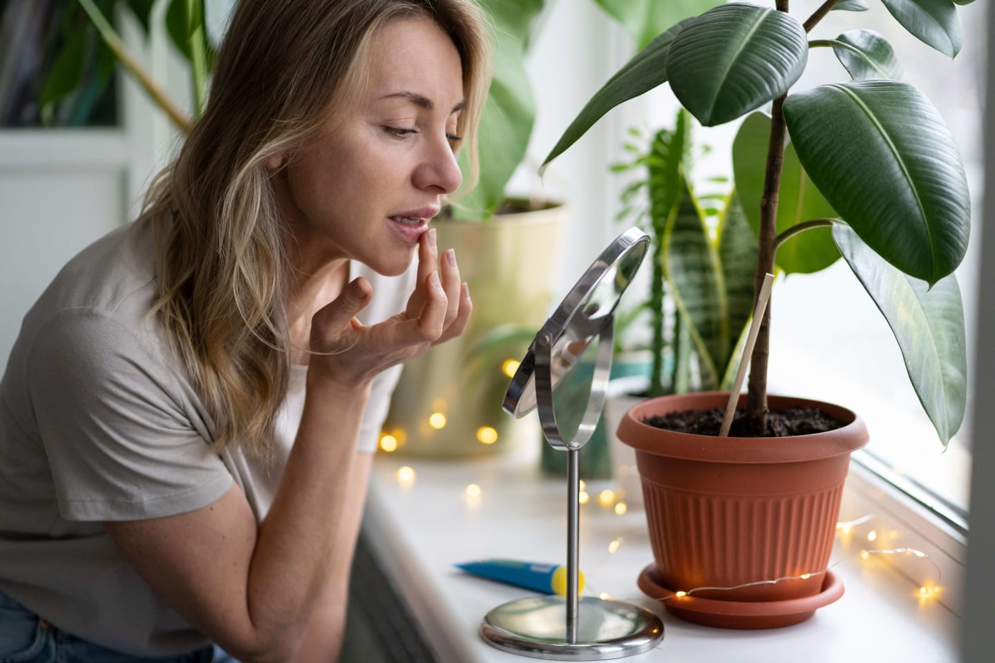 A woman applying lip balm in front of a mirror and house plants