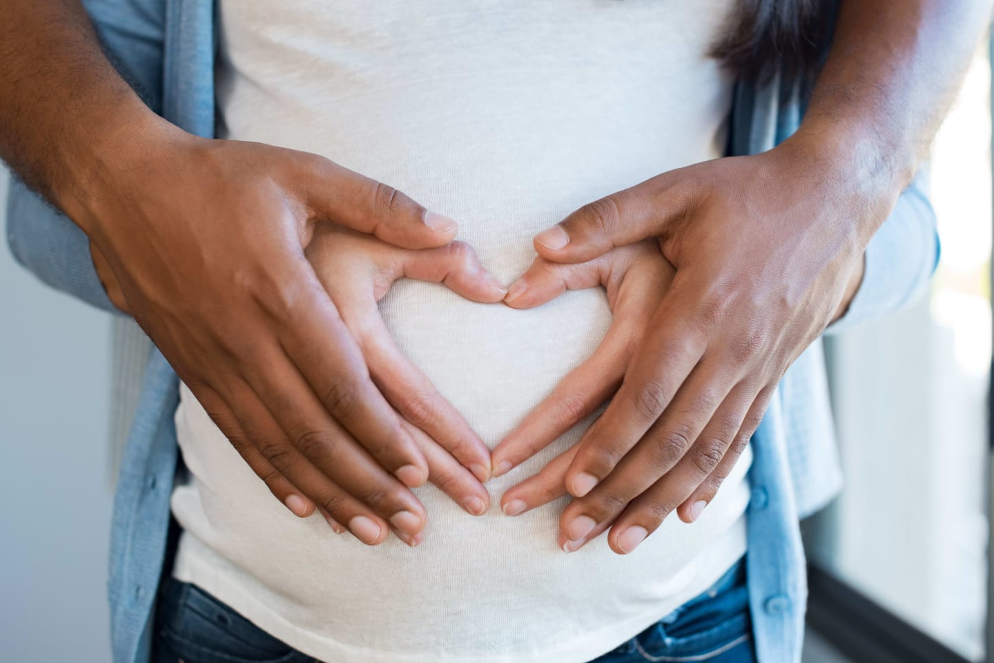A couple holding their hands over a pregnant belly to form a heart shape