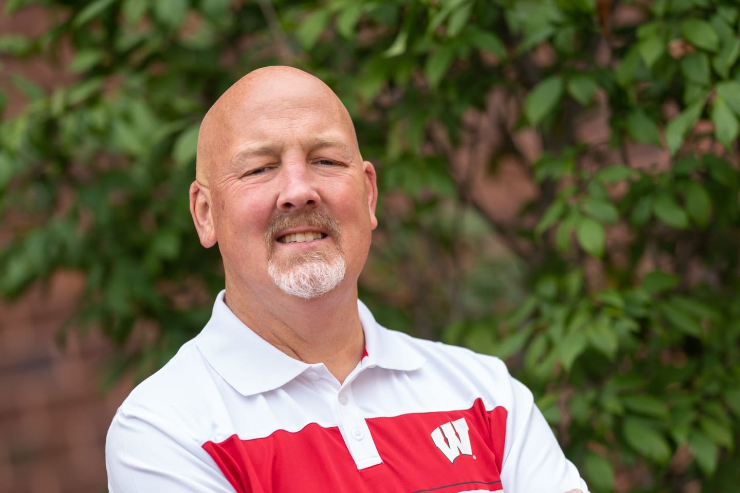 David Peterson standing with his arms crossed in a white Wisconsin Badgers polo