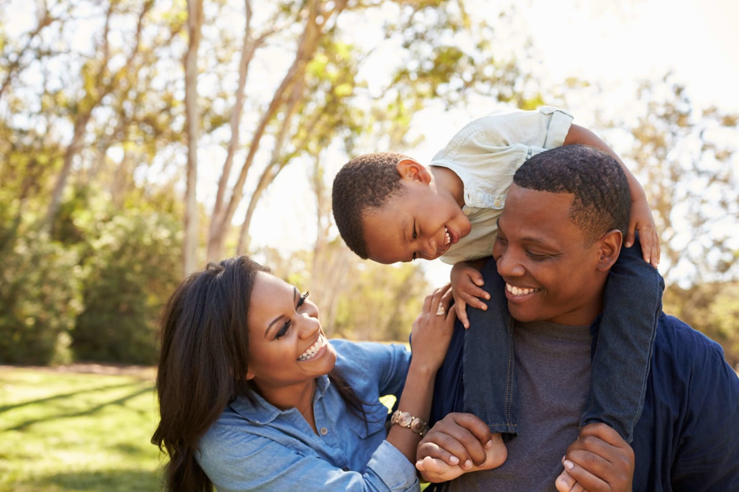 A family of three standing outside in a park smiling at each other