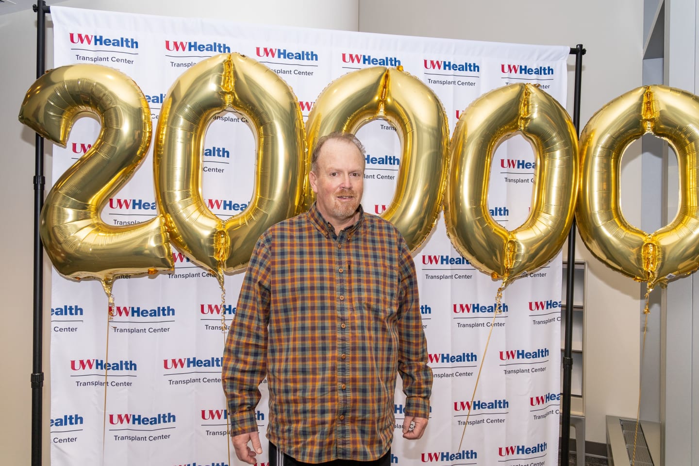 Man in a plaid shirt standing in front of balloons spelling twenty-thousand